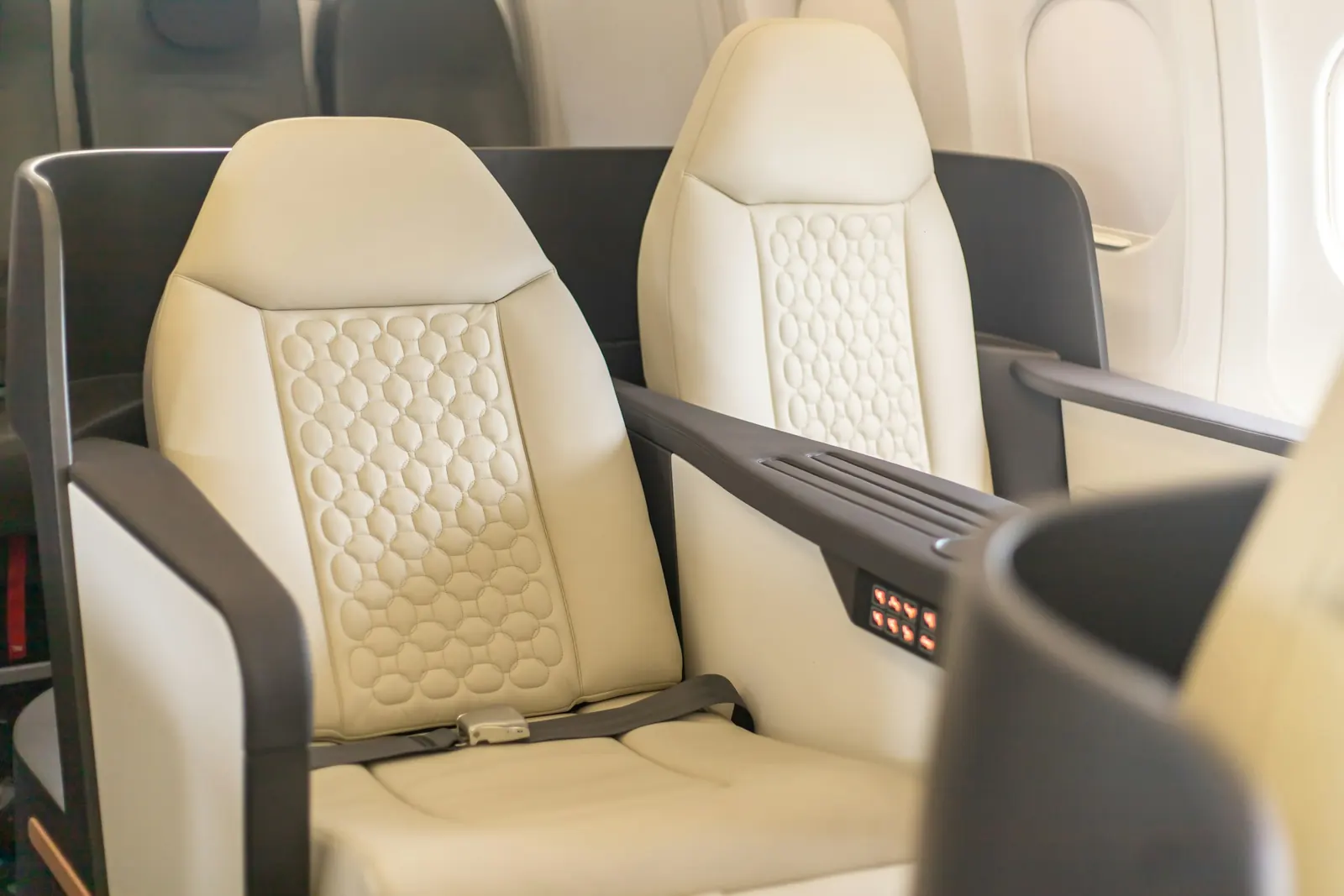 Cream leather first-class seats with a shared console on an airliner